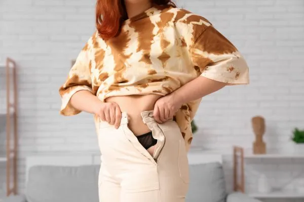 Image of woman trying to do her trousers up after pregnancy weight gain Camden