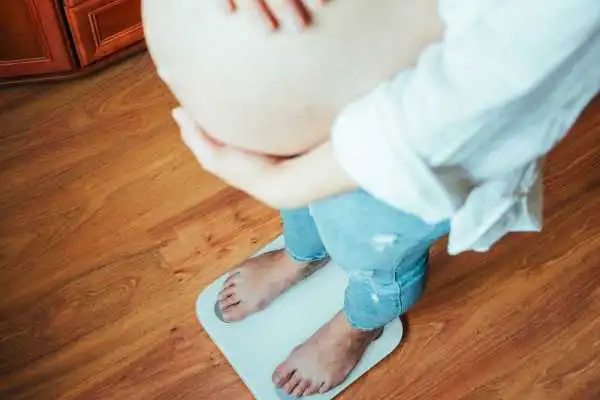 Image of woman weighing herself and experiencing weight gain through pregnancy Camden